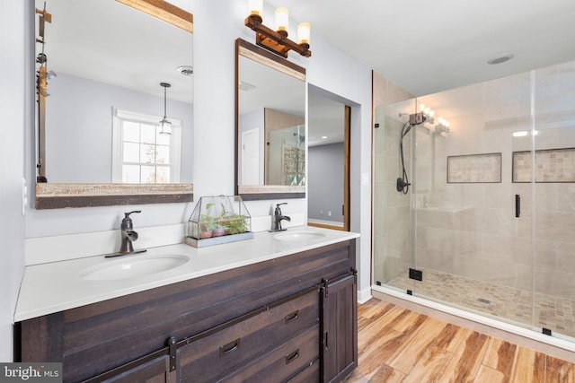 bathroom with double vanity, a shower stall, a sink, and wood finished floors