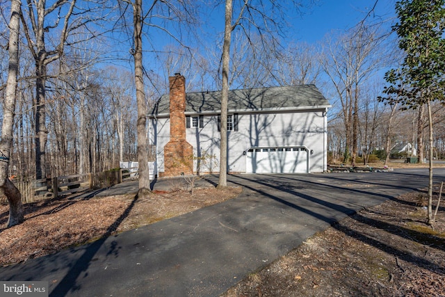 exterior space featuring driveway, a chimney, and an attached garage