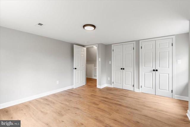 unfurnished bedroom featuring light hardwood / wood-style floors and two closets