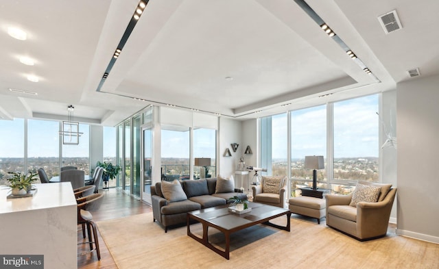 living room featuring light hardwood / wood-style flooring, a tray ceiling, a wall of windows, and a wealth of natural light