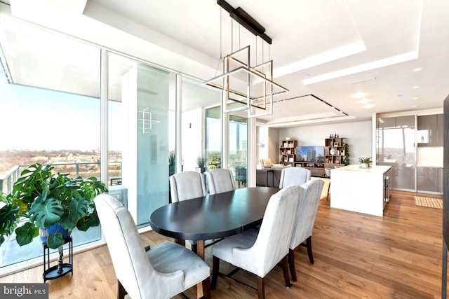 dining space featuring a notable chandelier, a tray ceiling, expansive windows, and hardwood / wood-style flooring