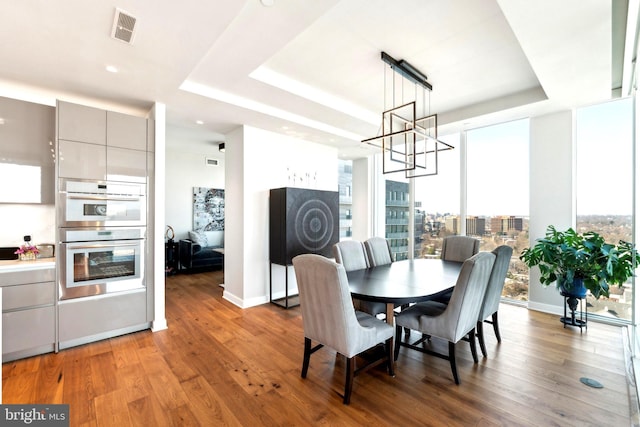 dining area with hardwood / wood-style floors, a wall of windows, and a tray ceiling