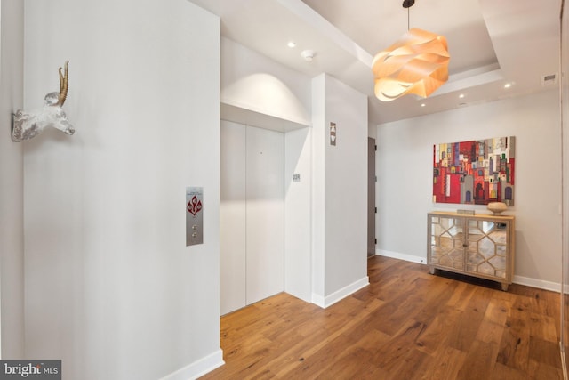 hallway with hardwood / wood-style flooring, elevator, and a raised ceiling