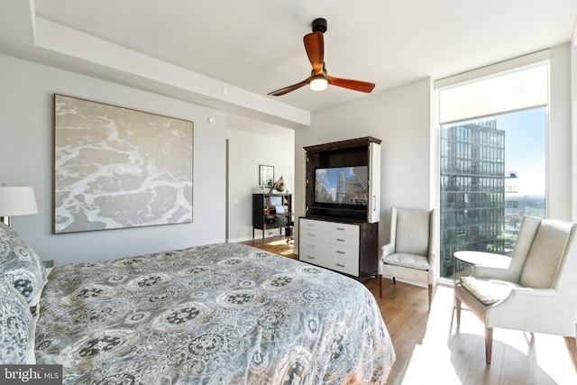 bedroom with expansive windows, wood-type flooring, and ceiling fan