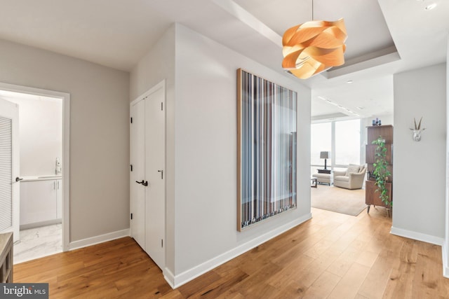 hall with a tray ceiling and light wood-type flooring