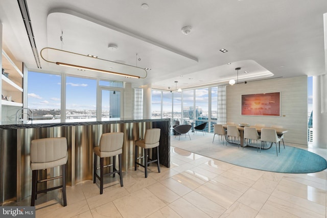 interior space with expansive windows, a water view, a kitchen breakfast bar, and a raised ceiling