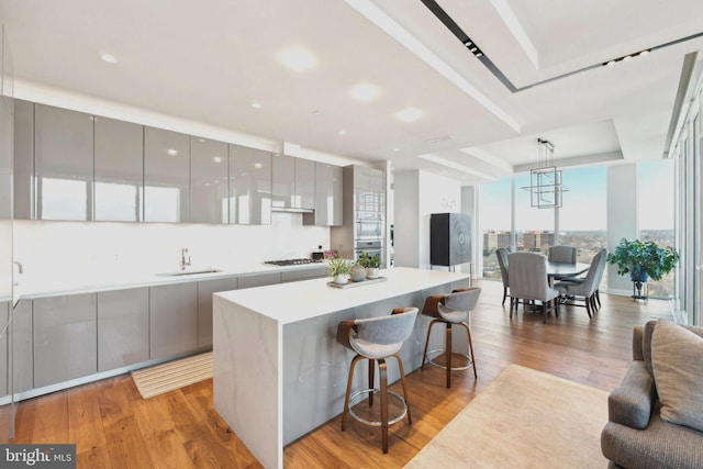 kitchen featuring sink, light hardwood / wood-style flooring, gray cabinets, hanging light fixtures, and a kitchen breakfast bar