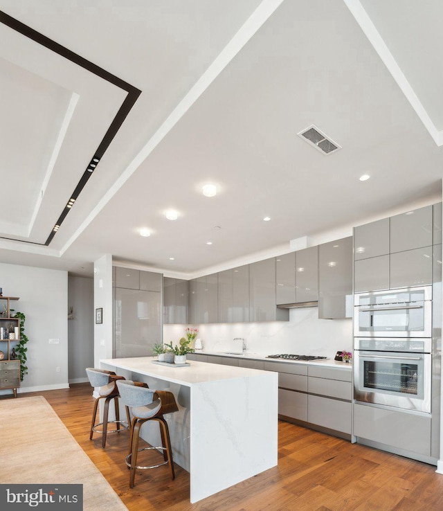 kitchen featuring a breakfast bar area, gray cabinets, a kitchen island, stainless steel appliances, and light hardwood / wood-style floors