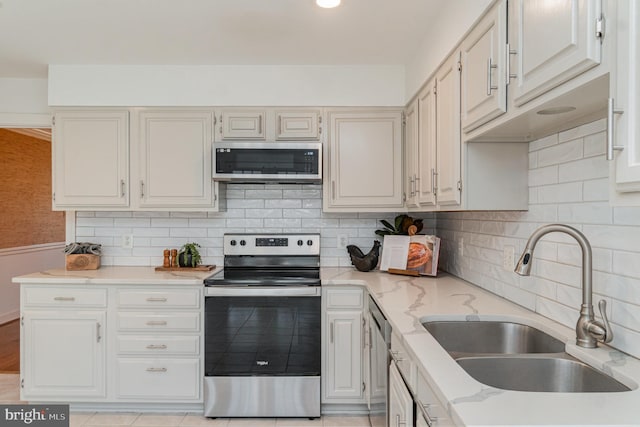 kitchen featuring sink, appliances with stainless steel finishes, white cabinetry, tasteful backsplash, and light stone countertops