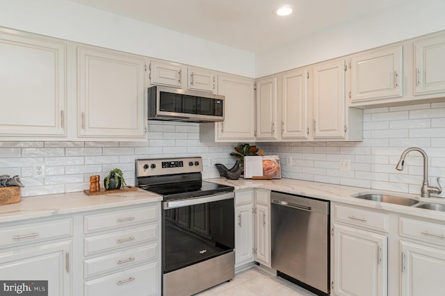 kitchen with sink, light tile patterned floors, stainless steel appliances, decorative backsplash, and white cabinets