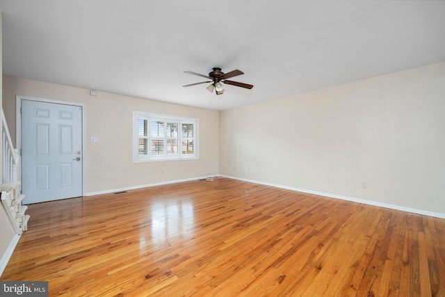 unfurnished living room with visible vents, stairway, light wood-style floors, ceiling fan, and baseboards