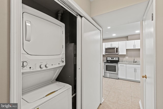 laundry room featuring light tile patterned flooring, stacked washer and clothes dryer, and sink