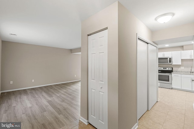 kitchen featuring stainless steel appliances, white cabinetry, light stone countertops, and light hardwood / wood-style flooring