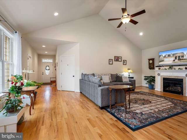 living room with a tile fireplace, high vaulted ceiling, ceiling fan, and light hardwood / wood-style floors