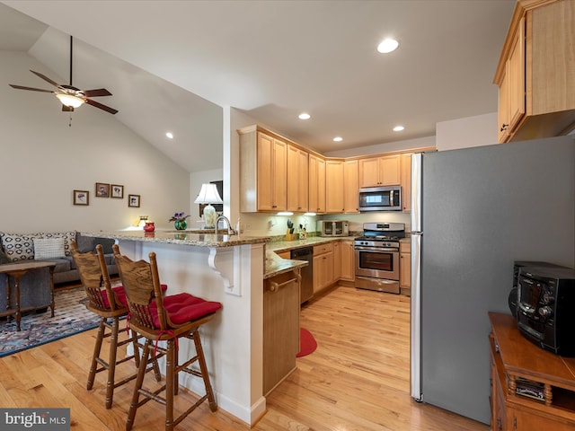 kitchen with appliances with stainless steel finishes, a kitchen breakfast bar, kitchen peninsula, light stone countertops, and light hardwood / wood-style flooring