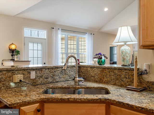 kitchen featuring lofted ceiling, sink, and light stone counters