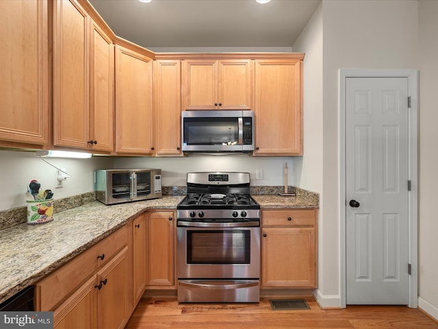 kitchen with stainless steel appliances, light stone countertops, and light wood-type flooring