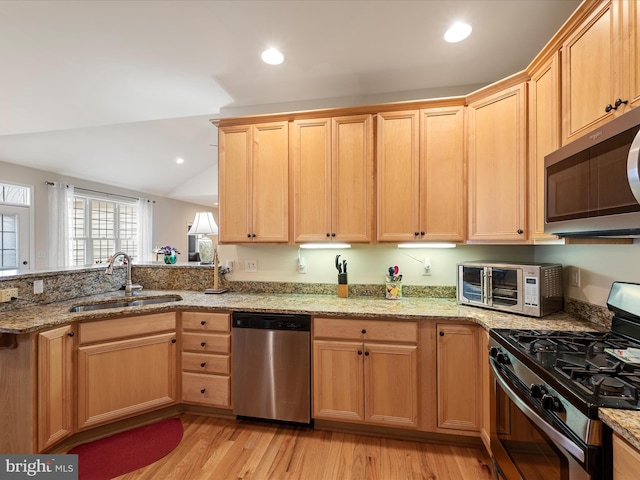 kitchen featuring lofted ceiling, sink, light stone counters, stainless steel appliances, and light hardwood / wood-style floors