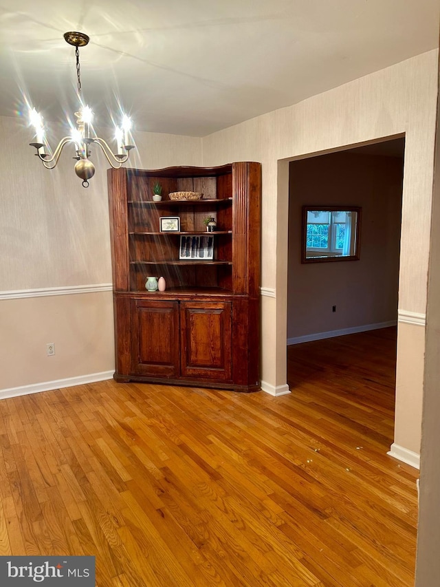 unfurnished dining area with wood-type flooring and a chandelier