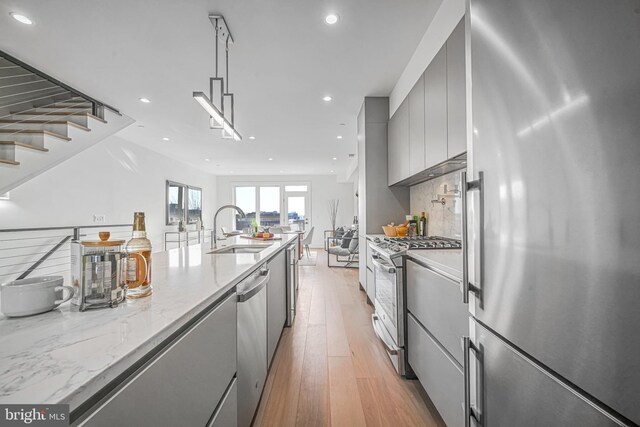 kitchen with sink, appliances with stainless steel finishes, light stone countertops, light hardwood / wood-style floors, and decorative light fixtures