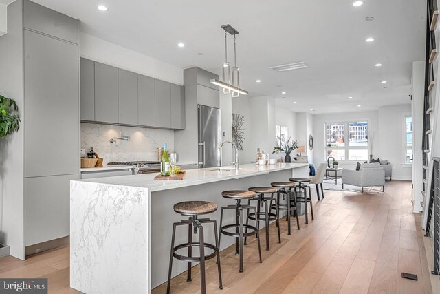 kitchen featuring a large island, a breakfast bar area, gray cabinetry, stainless steel appliances, and decorative light fixtures