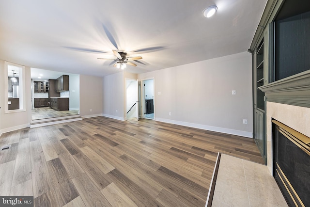 unfurnished living room with hardwood / wood-style flooring, a tile fireplace, and ceiling fan