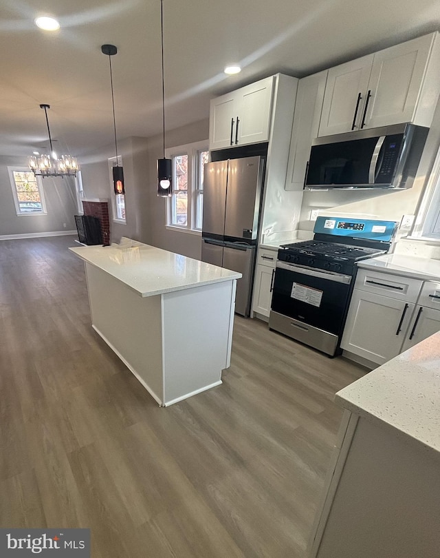 kitchen featuring stainless steel appliances, a kitchen island, pendant lighting, and white cabinets