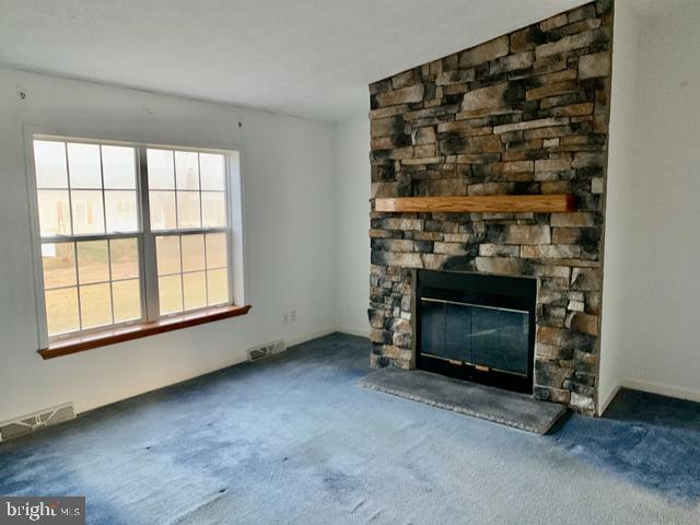 unfurnished living room featuring a stone fireplace and carpet flooring