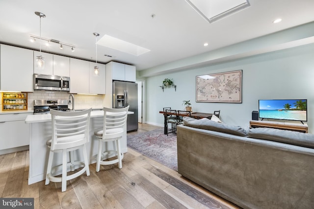 kitchen with appliances with stainless steel finishes, tasteful backsplash, white cabinetry, hanging light fixtures, and a center island with sink