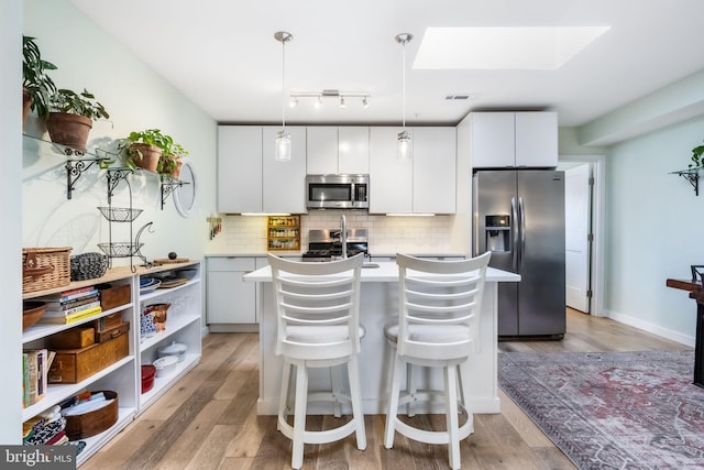 kitchen featuring appliances with stainless steel finishes, white cabinetry, hanging light fixtures, light hardwood / wood-style floors, and a center island with sink