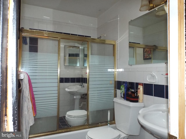 full bathroom with sink, tile walls, shower / bath combination with glass door, and toilet