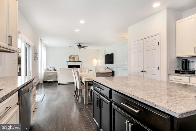 kitchen featuring tasteful backsplash, dark hardwood / wood-style flooring, dishwasher, light stone countertops, and white cabinets