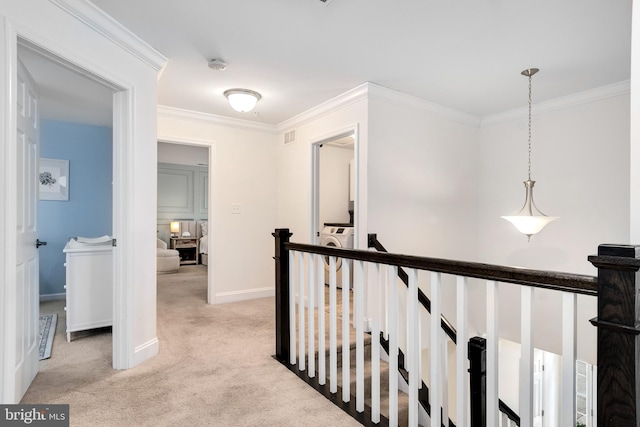 hallway featuring washer / dryer, crown molding, and light colored carpet