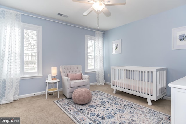 bedroom featuring a nursery area, light carpet, and ceiling fan