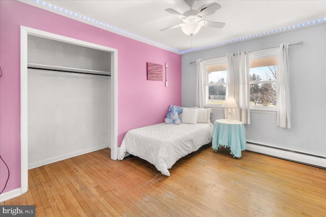 bedroom with a closet, ceiling fan, baseboard heating, and light hardwood / wood-style flooring