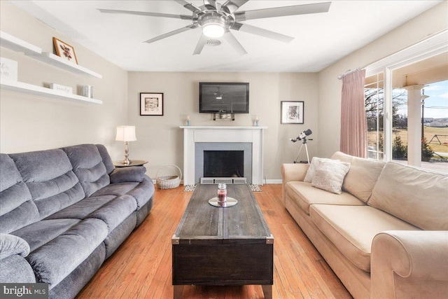 living room featuring a fireplace, light hardwood / wood-style floors, and ceiling fan