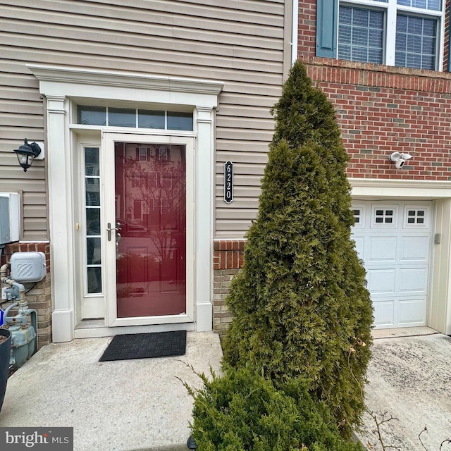 entrance to property featuring a garage and brick siding