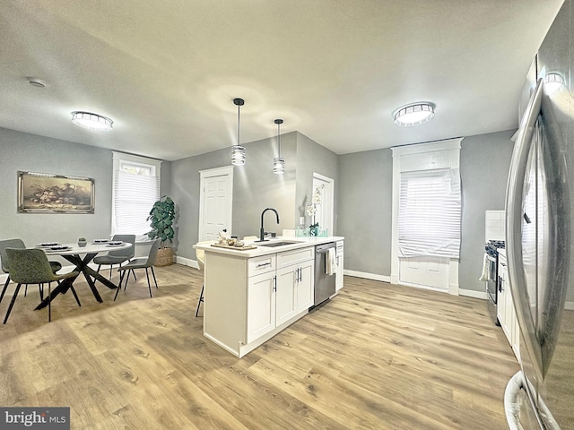 kitchen featuring sink, white cabinets, hanging light fixtures, stainless steel appliances, and light hardwood / wood-style flooring