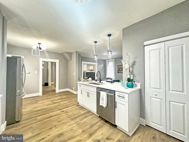 kitchen featuring sink, light hardwood / wood-style flooring, appliances with stainless steel finishes, white cabinetry, and decorative light fixtures