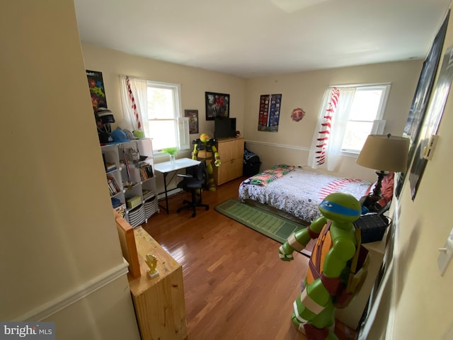 bedroom featuring hardwood / wood-style flooring, baseboard heating, and multiple windows