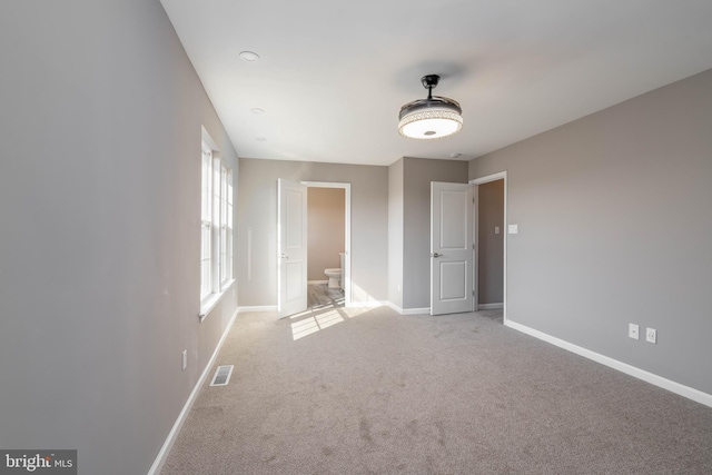 unfurnished bedroom with ensuite bath and light carpet