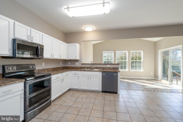 kitchen with appliances with stainless steel finishes, white cabinetry, sink, light tile patterned floors, and kitchen peninsula