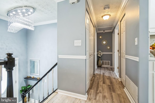 corridor featuring a textured ceiling, visible vents, light wood-type flooring, and an upstairs landing