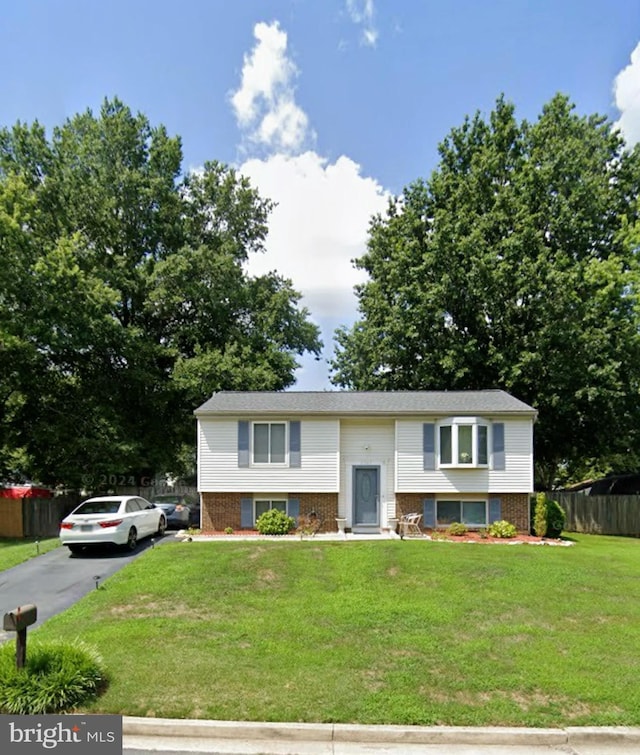 bi-level home featuring aphalt driveway, fence, a front lawn, and brick siding