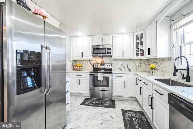 kitchen featuring light stone counters, appliances with stainless steel finishes, glass insert cabinets, white cabinetry, and a sink