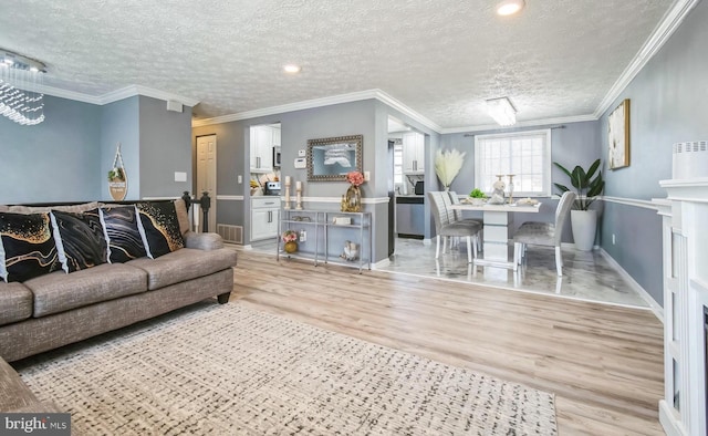 living area with a textured ceiling, light wood finished floors, ornamental molding, and visible vents