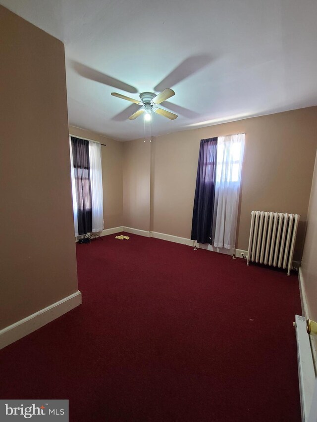 empty room with carpet floors, ceiling fan, radiator heating unit, and a healthy amount of sunlight