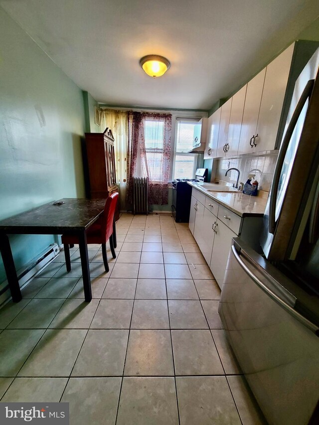 kitchen featuring light tile patterned flooring, sink, black refrigerator, white cabinets, and stove