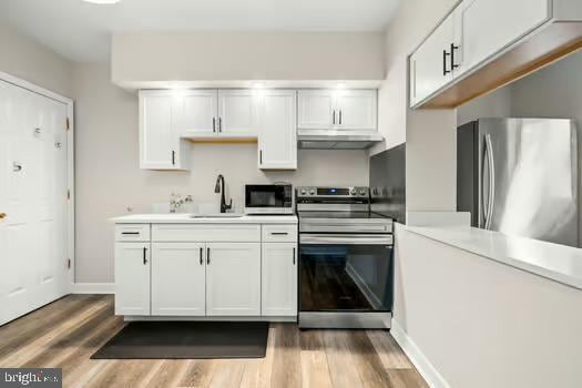 kitchen with stainless steel appliances, sink, hardwood / wood-style floors, and white cabinets