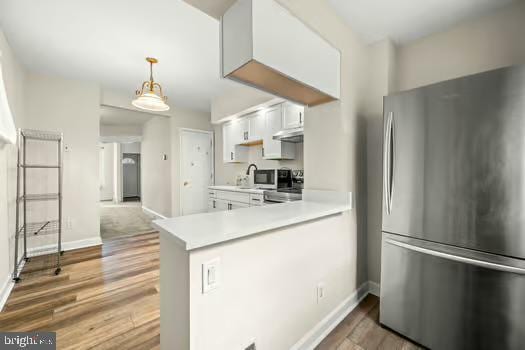 kitchen featuring dark wood-type flooring, stainless steel fridge, hanging light fixtures, white cabinets, and kitchen peninsula